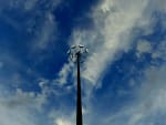 A tall high mast light stands against a dramatic sky filled with fluffy clouds