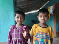 Two children stand together, smiling shyly at the camera