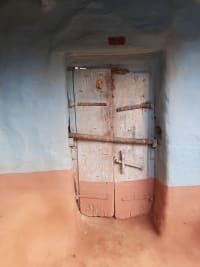 An Old wooden door with intricate iron hinges, nestled in a traditional mud-walled home, Kakadighi